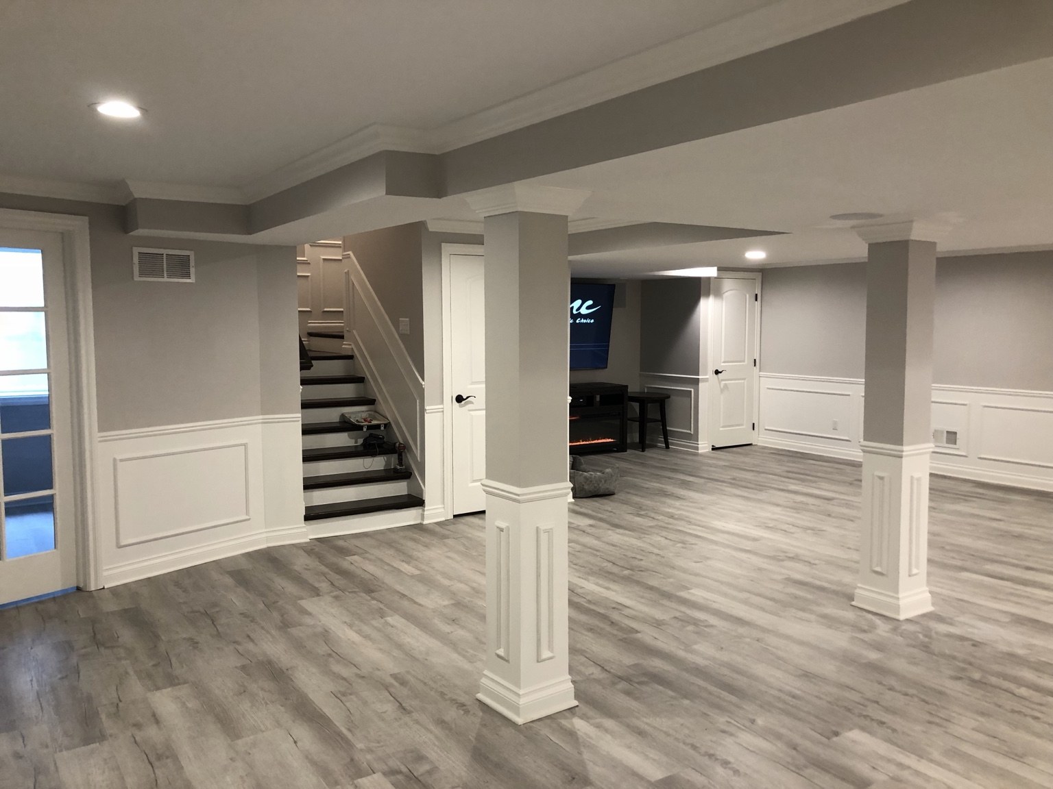Finished basement living space with paneled columns and staircase
