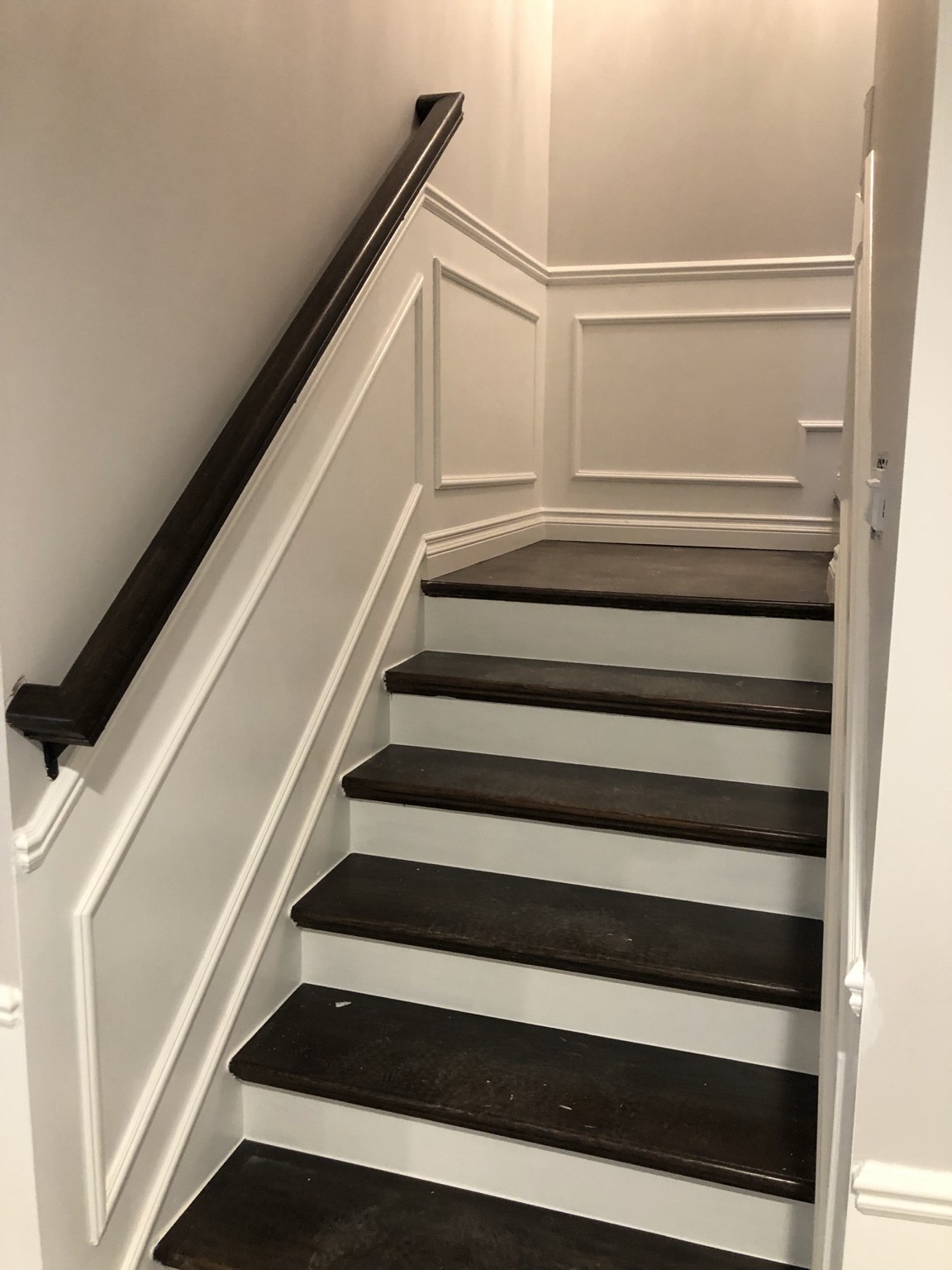 Staircase with dark wood treads and white wall panel molding