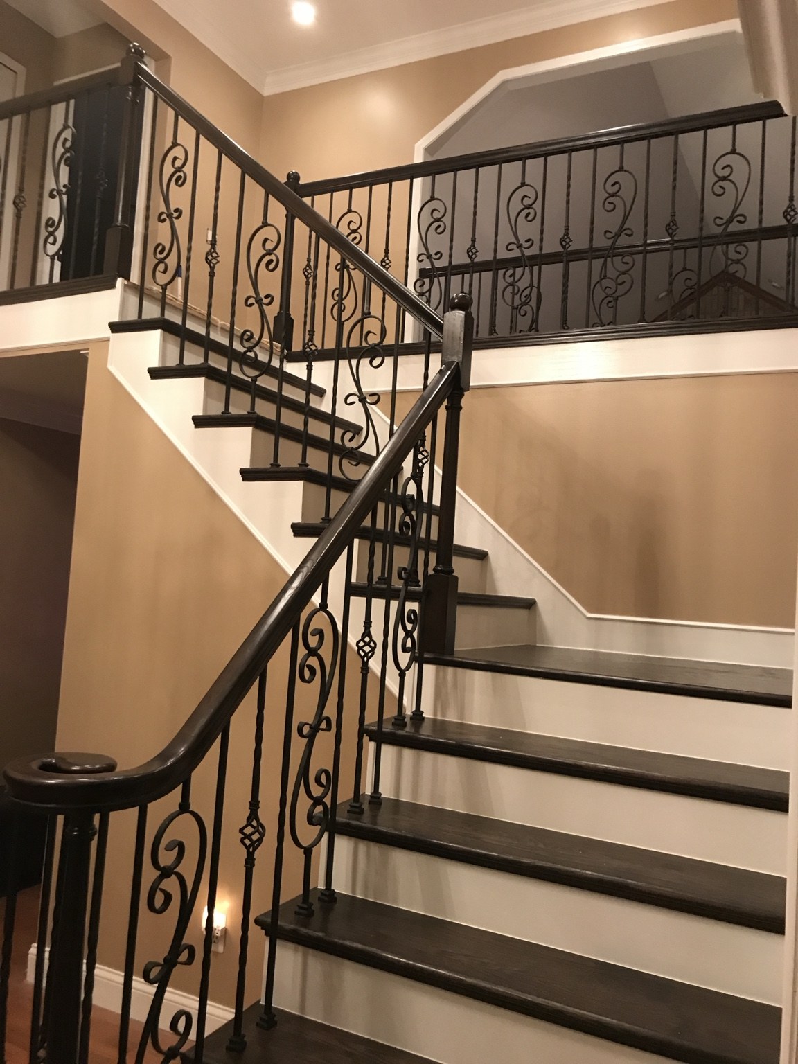 Staircase with dark wood treads, white risers, and ornate iron railing