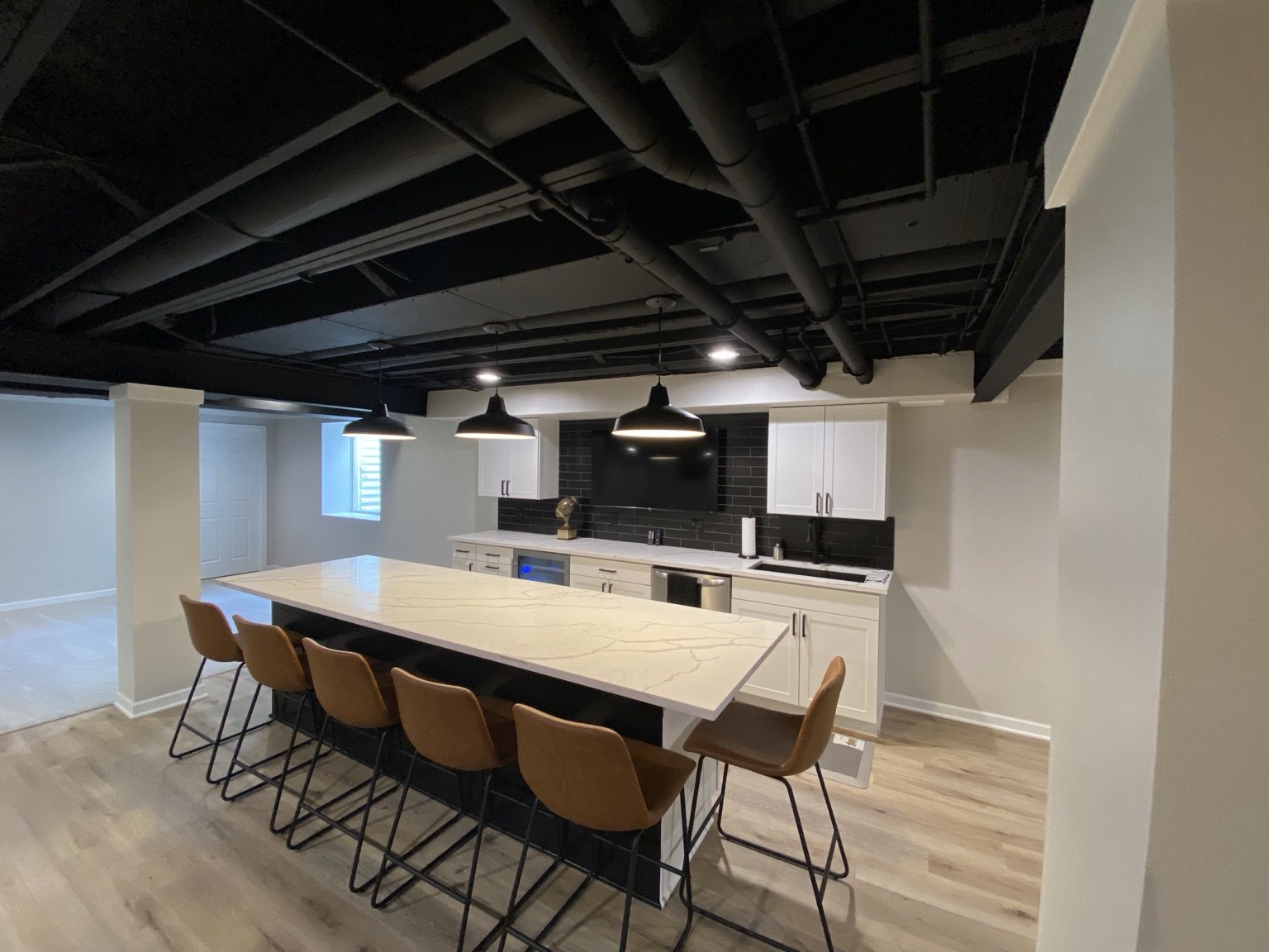 Basement bar with white cabinets, pendant lights, and island seating