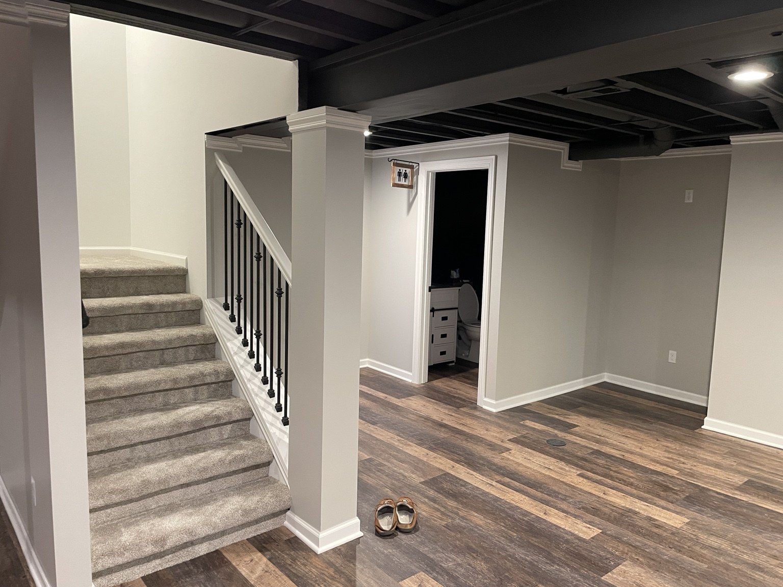 Basement staircase with black spindles beside bathroom entrance