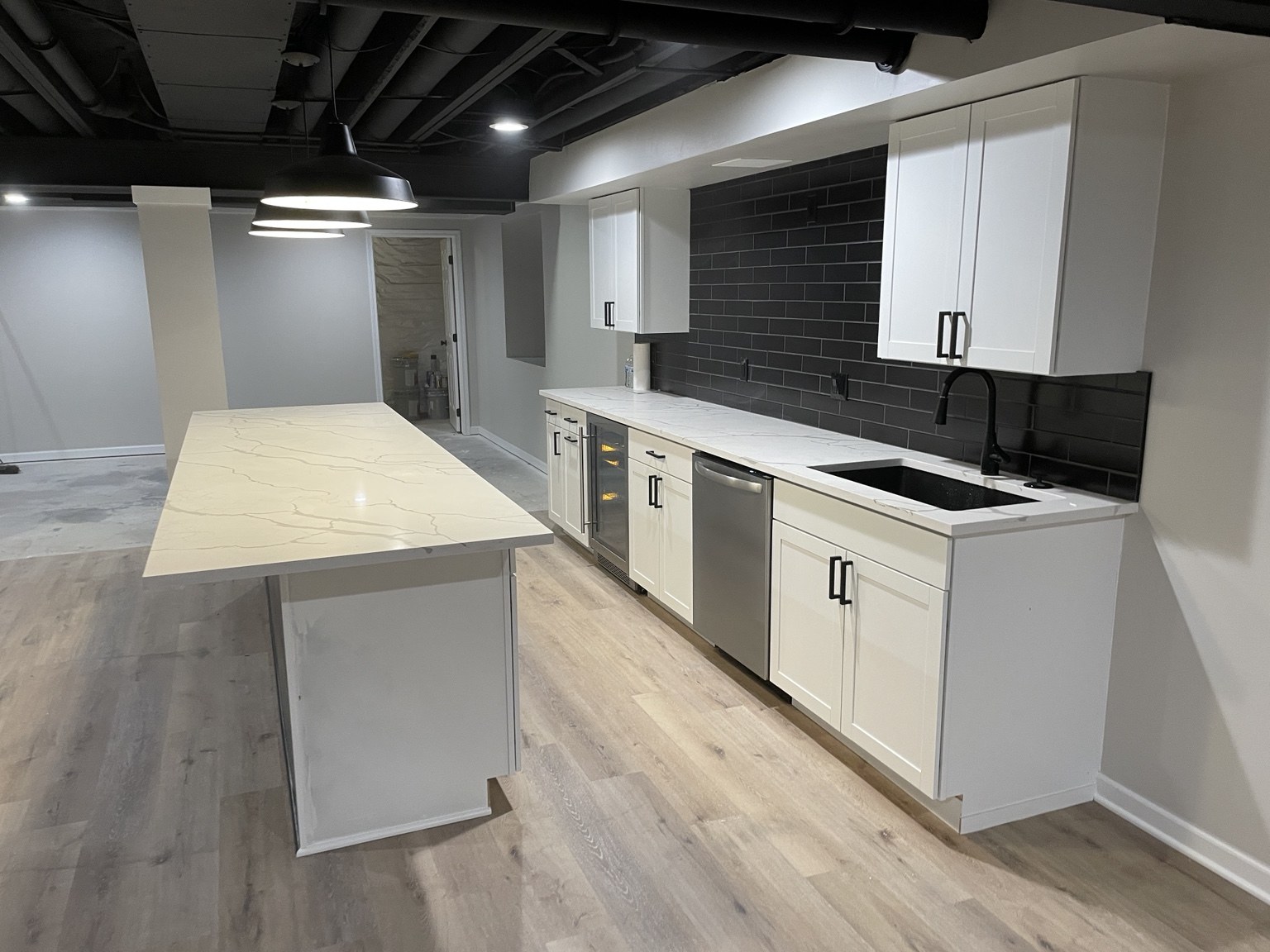 Basement wet bar with white cabinets and dark tile backsplash